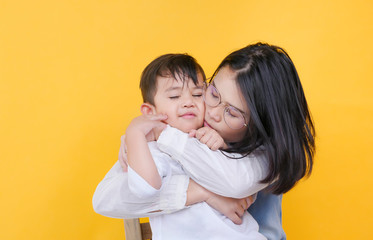 Loving mother and son hugging in studio over yellow background.