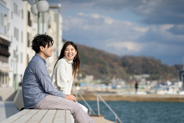 Fototapeta premium 堤防に腰掛け楽しそうに会話をする若いカプル