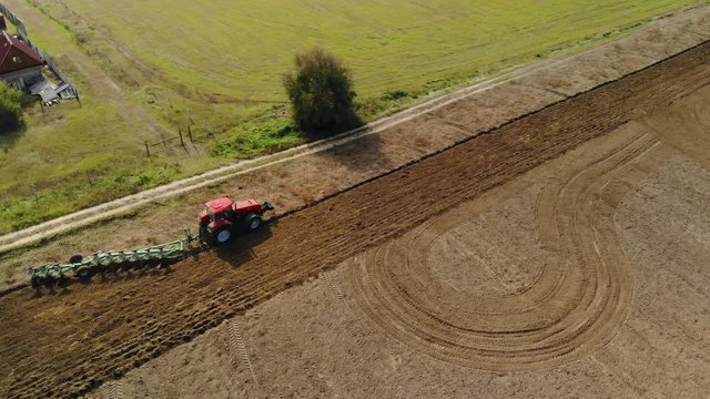 The red tractor uses a seeder-cultivator to prepare the soil in early spring. Agricultural work on large, fertile land. Top view from the drone. Beautiful picture, the texture of the dark field and
