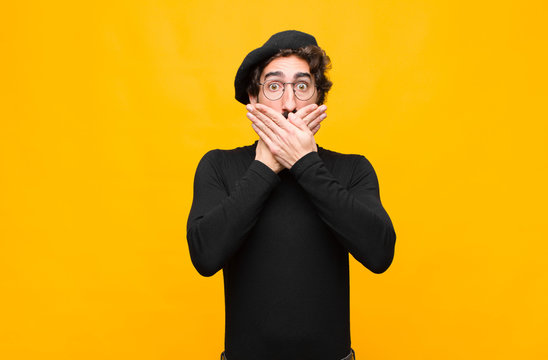 young french artist man covering mouth with hands with a shocked, surprised expression, keeping a secret or saying oops against orange wall