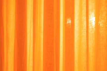 Translucent textile monochrome orange curtains and a beam of light radiating through them