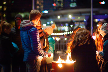 Naklejka premium A group of young people is warming around the fire on the waterfront in Docklands. Winter, city life in Melbourne. Darkness.