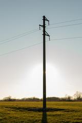 Fototapeta na wymiar Selective focus. A line of electric poles with cables of electricity in a field with a forest in background in autumn during sunset.