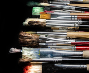 different used paint brushes on a black background