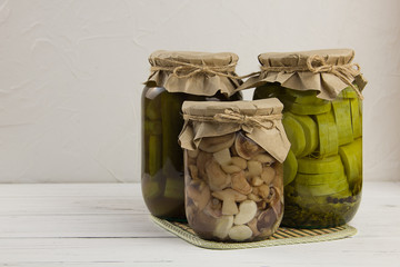 canned fermented mushrooms cucumbers and zucchini in a bank on a light wooden background