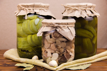 fermented pickled canned zucchini and cucumber mushrooms in jars garlic bay leaf black pepper peas on a piece of burlap on a brown wooden background