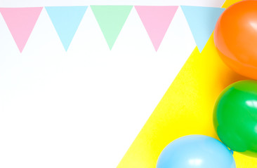 Colorful garland of paper triangles and multi-colored balloons on a double yellow and white background. Greeting card. Flat lay style. Copyspace for text.