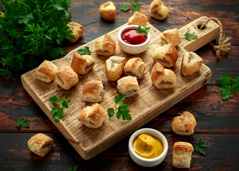 Pork sausage rolls with mustard and ketchup sauce on wooden board