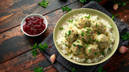 Hot Swedish meatballs with white rice and cranberry sauce on wooden table