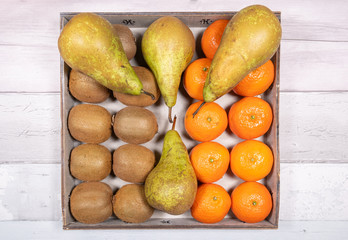 Bananas, conference pears, tangerines and kiwis placed in an old wooden tray on a background of old wooden floor