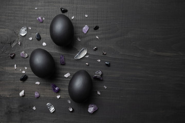 Eggs painted black with multi-colored stones. Eggs on a black wooden background. Preparing for Easter. Cooking food.