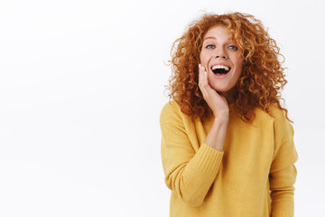 Happy smiling redhead woman with curly hair, wear yellow sweater, laughing and touching face surprised and pleased, glad see got rid acne, satisfied after cosmetics procedure, white background