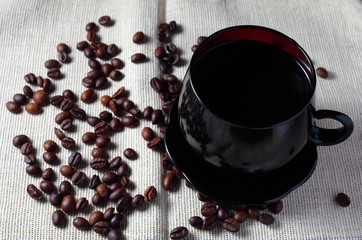 dark coffee mug on a background of burlap with scattered grains of coffee on the table close-up