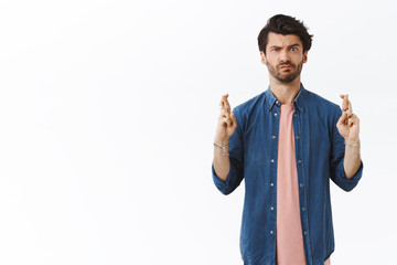 Intense, skeptical handsome man cross fingers good luck but have doubts if dream come true,...