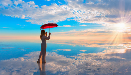 Young girl in dress holding red umbrella and walking on the salt lake
