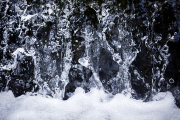 Close up of waterfall stream and drops with foamy bottom on summer day background, texture and wallpaper