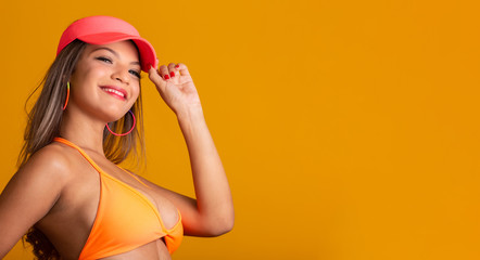 Attractive girl in a orange bikini, hat, emotionally opened mouth on a bright yellow background with a perfect body. Isolated. Studio shot.