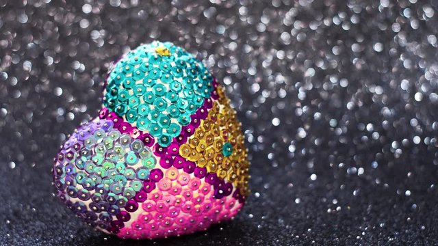Heart in multicolored sequins on a black luminous background. Video by heart.