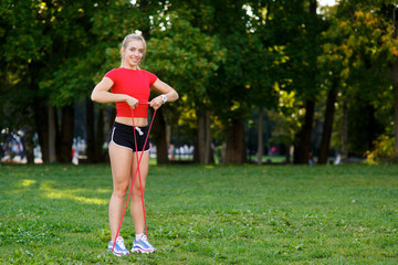 Young woman is training with rubber bands outdoors. Healthy active lifestyle concept. girl doing fitness in the park on the nature