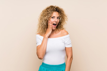 Young blonde woman with curly hair over isolated background with surprise and shocked facial expression