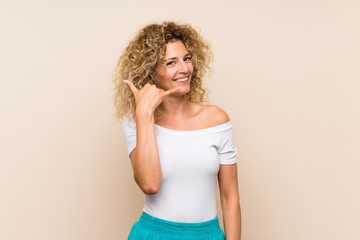 Young blonde woman with curly hair over isolated background making phone gesture. Call me back sign