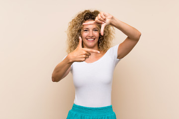 Young blonde woman with curly hair over isolated background focusing face. Framing symbol