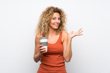 Young blonde woman with curly hair holding a take away coffee with shocked facial expression