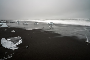 Crystal clear and blue ice chunks washes up on the black lava sand by the waves on diamond beach in Jokulsarlon glacier lagoon. Climate change and glacier melting concept.