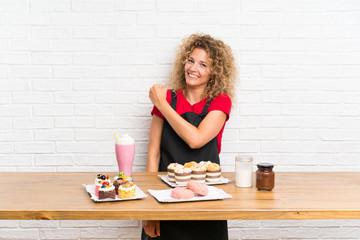 Young woman with lots of different mini cakes in a table celebrating a victory