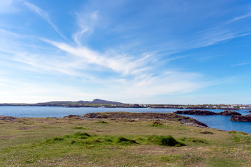 A view of the coastline at  Treasurer bay, Anglesey.  In the far distance is Holyhead mountain, and in the foreground is the rock sea shore.  A bright, sunny, summers day.