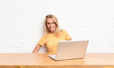 young blonde woman smiling cheerfully and casually with a positive, happy, confident and relaxed expression using a laptop © kues1