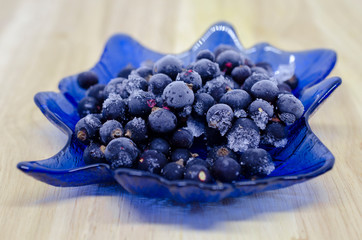 frozen blackcurrant berries lie on blue glass plate in the form of a tree leaf