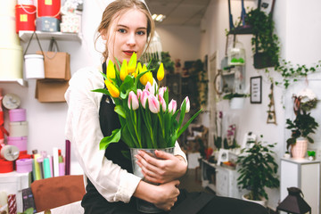 Portrait of a flower seller with tulips in hands. Young floristry works in a flower shop