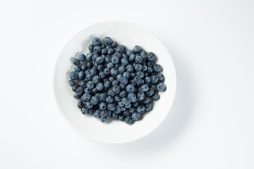 Ripe blueberries in a white plate on a white background top view.