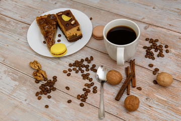 Cup of coffee and two slices of cake and macaroons on the plate on wooden table