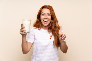 Teenager redhead girl holding a glass of milk over isolated background pointing up a great idea