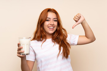 Teenager redhead girl holding a glass of milk over isolated background proud and self-satisfied