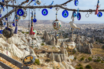 Evil Eye Beads on Tree and Fairy tale chimneys on background of blue sky in Pigeons Valley,Goreme,Turkey.Branches of the old tree decorated with the eye-shaped amulets Nazars Evil eye made of blue gla - obrazy, fototapety, plakaty