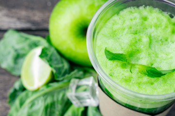 Green apple smoothie in glass and kale leaves on wooden table