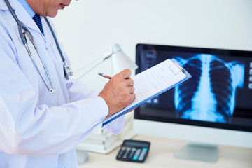 Unrecognizable male doctor wearing white coat making notes in medical record, horizontal shot