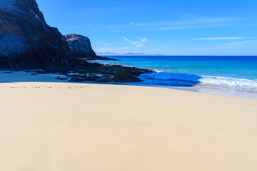 View of beautiful Playa de la Cera beach, blue sea, yellow sand, cliffs. Papagayo, Playa Blanca, Lanzarote, Canary Islands. VIew of Fuerteventura on the background, selective focus