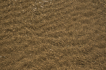Sea bottom texture, yellow sand waves in shallow water. The sun glare from the water on the sand