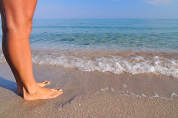 Fototapeta na wymiar Beautiful female legs near sea waves on a sandy beach