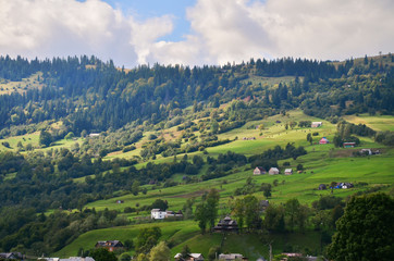 Sunrise, the sun's rays illuminate the beautiful panorama of the Carpathian village against backdrop of scenic mountains, where the highlanders live Hutsul. Wild forests, fields pastures. 