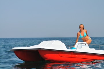 Young woman in bikini standing on white catamaran in sea and smiling