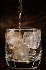 pour whiskey in a glass with ice on a dark wooden background close-up
