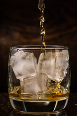 pour whiskey in a glass with ice on a dark wooden background close-up
