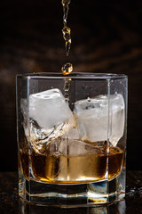 pour whiskey in a glass with ice on a dark wooden background close-up