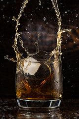big splash in a glass with whiskey with ice on a dark wooden background