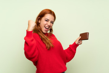 Naklejka premium Teenager redhead girl with sweater over isolated green background holding a wallet